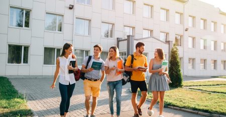 Five friendly students are walking after they passed test outside the college building and discuss the project